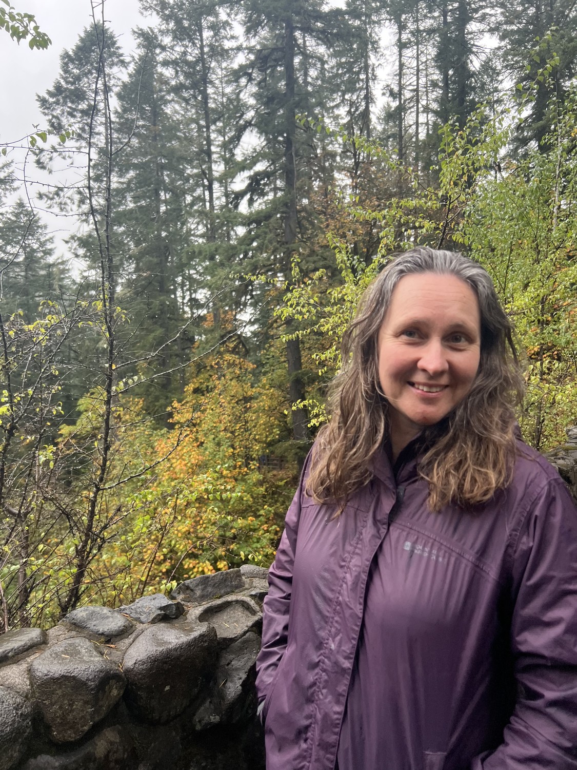 Tamara smiling in a forest, wearing a purple jacket